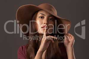 Its our little secret. Cropped portrait of an attractive young woman posing with her finger on her lips in studio against a grey background.