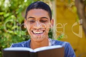 I never start my days without reading my bible. a handsome young man sitting alone outside and reading a book during the day.