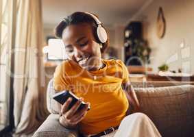 Young woman texting, browsing and scrolling social media on a phone feeling happy, carefree and smiling. Listening to music, podcast or watching funny internet memes online while relaxing on a sofa