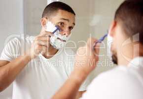 The ladies love a smooth face. a young man looking at his reflection as she shaves his face.