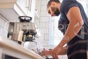 Theres nothing as luxurious as a foamy cappuccino. a young man wiping down the milk frother on his coffee machine.