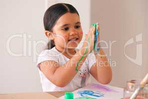 Shes having a blast. an adorable little girl smearing water-based paint on her hands.