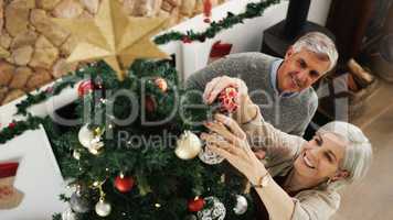 Deck the halls with love and laughter. a happy senior couple decorating their Christmas tree at home.