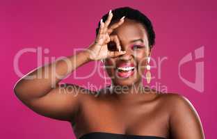 Born to stand out not to blend in. Studio shot of a beautiful young woman looking through her fingers against a pink background.