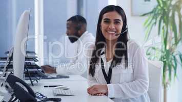 Its always a pleasure to help our clients further. Portrait of a young businesswoman working on a computer in a call centre with a colleague in the background.