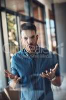 Angry, stressed and frustrated man unhappy and feeling bad about work problems while standing in a modern office alone. Aggressive, annoyed and upset young male filled with emotions screaming loud