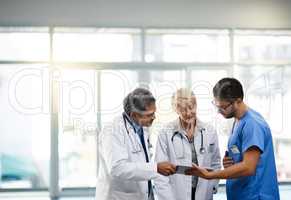 Team or group of doctors, nurses and medical professional talking, meeting and discussing healthcare in a hospital. Health practitioners in labcoats looking at records on a tablet in a clinic