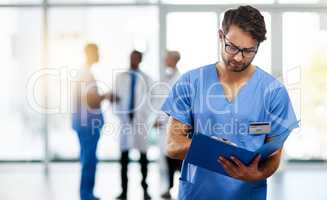 Doctor, healthcare professional and medical worker reading, holding and looking at health information and records in a hospital. Practitioner with a clinic file and colleagues in the background