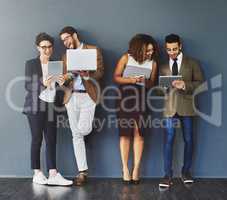 Happy workers using digital devices standing together on a work break. Group of relaxed employees using technology, a phone, computer and tablet. Office business team enjoying social media indoors