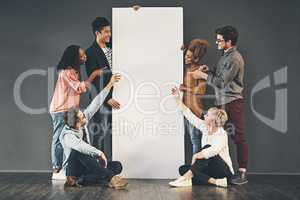 A diverse group of people holding a blank white board or poster and showing advertising copy space. A team or friends marketing a placard banner standing and sitting together for a promotion