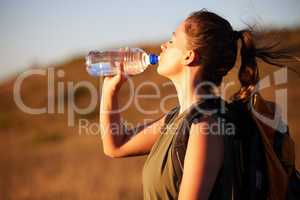 You wont get bored of hiking but you will get thirsty. a young woman drinking water while out for a hike.