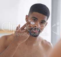 I dont wake up looking this good without my skincare routine. Cropped portrait of a handsome young man standing and using his bathroom mirror to apply moisturizer on his face.