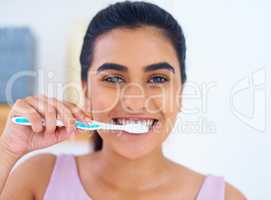 Keeping her bright smile in mint condition. Portrait of a young woman brushing her teeth at home.