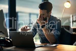 Struggling with occupational stress. Shot of a young businessman experiencing stress during a late night at work.