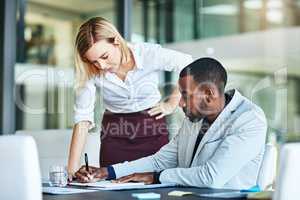 Business people working together in a modern office, writing and reading paperwork. Director training an assistant and helping him with his report. Woman coaching a new employee at work