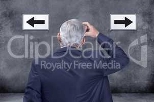 A rear view of thinking, confused and deciding businessman struggling and trying to decide which way to go. Indecisive corporate worker chooses direction with left and right arrow sign on black wall