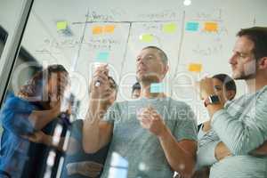 Business people brainstorming, planning and thinking of ideas on a glass board. A group or team of young professional designers using sticky notes to organize their thoughts in a modern office.