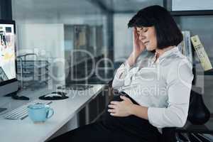 This is the worst time to be in the office. an attractive businesswoman sitting and feeling stressed while holding her pregnant tummy in the office.