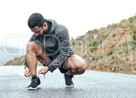 You cant boost your performance if youre not fully prepared. a sporty young man tying his shoelaces while exercising outdoors.