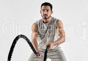 Strength comes from an indomitable will. Studio shot of a muscular young man exercising with battle ropes against a white background.