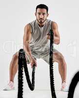 Keep calm and hiit it. Studio portrait of a muscular young man exercising with battle ropes against a white background.