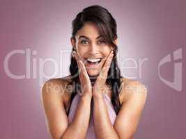 The unexpected moment is always sweeter. a beautiful young cheerful woman with her hands rested on face against a pink background.