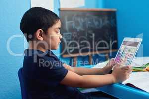 Its no substitute for a teacher but its pretty close. an adorable little boy using a digital tablet to complete a school assignment at his desk.