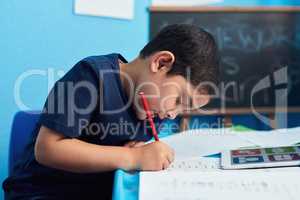 The smallest task can teach the biggest lesson. an adorable little boy completing a school assignment at his desk.