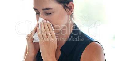 Her allergies are flaring up again. a young businesswoman blowing her nose in an office.