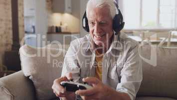 Ive got it all under control over here. a senior man sitting alone on the sofa at home and wearing headsets while gaming.