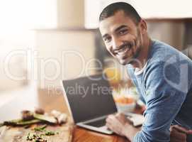 Young man on a laptop while preparing a healthy meal at home. Portrait Happy smiling male browsing and learning on computer in the kitchen on how to cook. Guy alone checking online recipes on the web