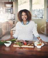 Portrait of happy black woman preparing healthy food in a kitchen at home. Young African American using fresh vegetables to make a delicious, balanced low carb meal. Lady on a cleanse and detox diet