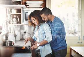 Loving and affectionate couple cooking breakfast, lunch or dinner together in the kitchen while hugging. Young Black American lovers preparing a meal at home on a fun weekend enjoying quality time