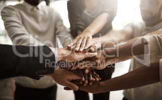 Businesspeople with their hands together in a huddle pile showing support, teamwork and close collaboration at the workplace. Closeup of a diverse group of colleagues standing in unity at the office