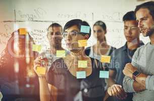 Business people planning ideas on a glass board thinking, brainstorming and working on strategy for a project. Smart, busy and organized workers doing work schedule brainstorm with sticky notes