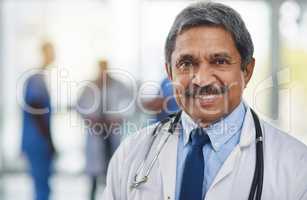 Doctor, medical professional and healthcare worker with smiling, happy and friendly face expression and hospital colleagues in background. Closeup, portrait and headshot of mature clinic specialist