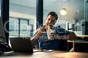 Young hungry businessman working late and eating at desk. Man having takeout food in the office at work station in the evening. Male entrepreneur eating asian meal during the night at the workplace