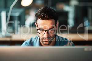 Serious business man working at computer late in the office at night to finish reports, articles or code. Focused and young male IT worker wearing glasses late in the evening for deadline