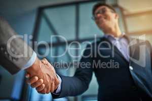 A professional handshake after a successful group collaboration meeting after in a modern corporate office. Young man shaking customers hands after sealing a business contract deal for the company
