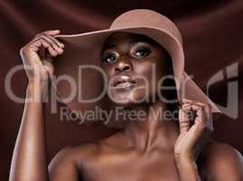Your skin is your best accessory, take care of it. a beautiful young woman wearing a hat while posing against a brown background.