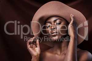 Say bye to dull skin and hello to glowing skin. a beautiful young woman wearing a hat while posing against a brown background.