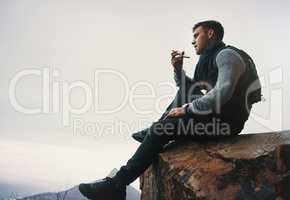 Enjoying the weekend by escaping the ordinary. a young man talking on a cellphone while sitting on a mountain cliff.