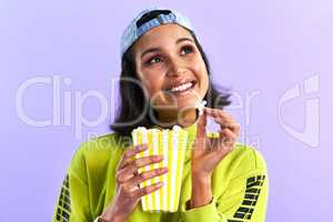 The most memorable movies make a lasting impact. Studio shot of a beautiful young woman eating popcorn against a purple background.
