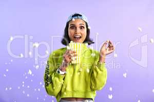 Kernel popping, heart stopping, action packed movies. Studio shot of a beautiful young woman eating popcorn against a purple background.