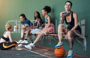 Chilling after another victory. Full length portrait of an attractive young female athlete sitting on a bench at the basketball court with her teammates in the background.