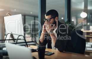 I wish I was at home right now. a young businessman feeling stressed while working late at night in a modern office.