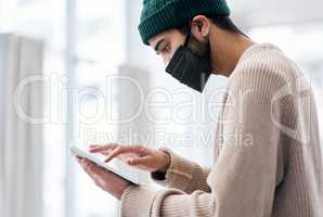 Work must go on. a masked young man using a digital tablet while working from home.
