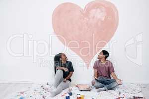 Fill your home with lots of love. a young couple painting a heart on a wall.