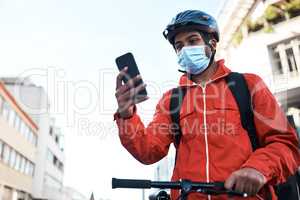Checking the route to his delivery address. a masked man using his cellphone while out on his bicycle for a delivery.