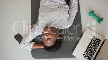 Be active, be healthy, be happy. High angle shot of a young woman lying on an exercise mat with a laptop, cellphone and dumbbell around her.